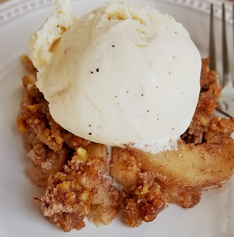 Healthy apple crisp topped with vanilla ice cream on white plate