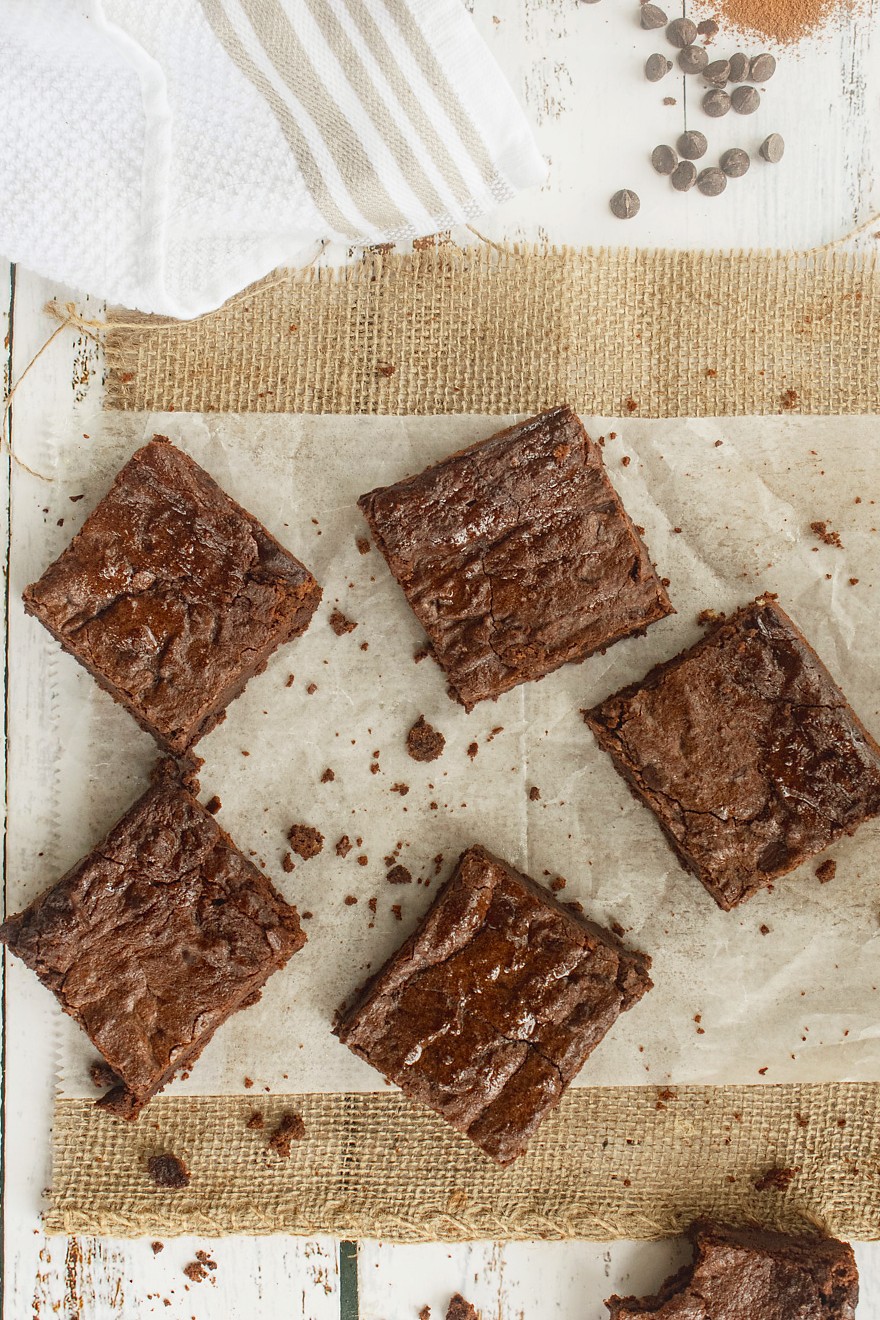 Overhead view of fudgy low carb brownies with crackly top on parchment with chocolate chips and cocoa