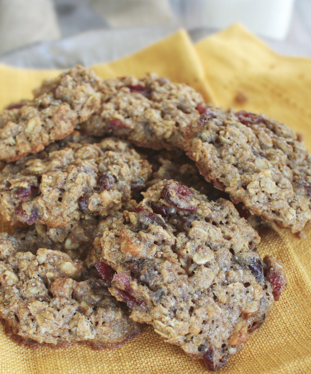 Soft chewy healthy oatmeal cookies with craisins piled on yellow napkin next to glass of milk