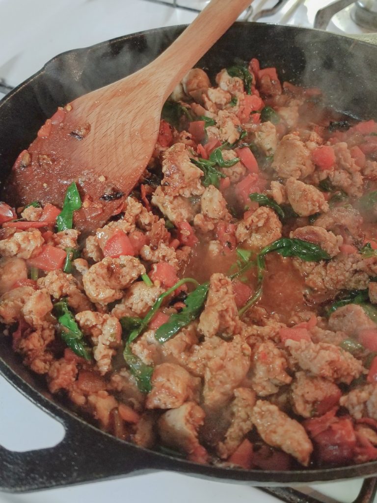 sausage, tomato and spinach cooking on stove